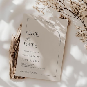 Plain, bright white, sheet background with shadows a sprig of a dried tree branch  - it gives boho, nature vibe without too much clutter. In the center of the mock up is a plain white wedding save the date card - it has elegant, cursive scripts. Under the card appears to be a bundle of sage or brown plant material in a boho presentation.This card has a few different fonts that actually make up the border in an unique, modern style. The card itself if black and white.