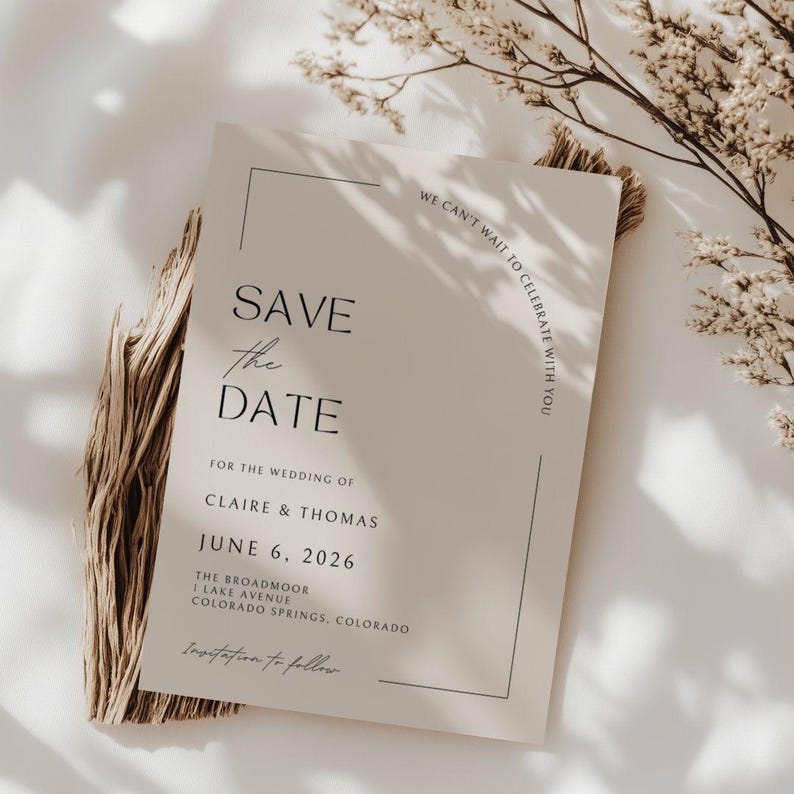 Plain, bright white, sheet background with shadows a sprig of a dried tree branch  - it gives boho, nature vibe without too much clutter. In the center of the mock up is a plain white wedding save the date card - it has elegant, cursive scripts. Under the card appears to be a bundle of sage or brown plant material in a boho presentation.This card has a few different fonts that actually make up the border in an unique, modern style. The card itself if black and white.