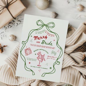 This is a winter mockup photo of Christmas scene -white colored, knit sweater, a a brown package,  and neutral color ornaments. In the center of the mockup is a Winter themed Bachelorette invitation. The invite is white, red, and green with hand drawn cocktails and a doodle style font - the large red green bow as the border makes it unique.