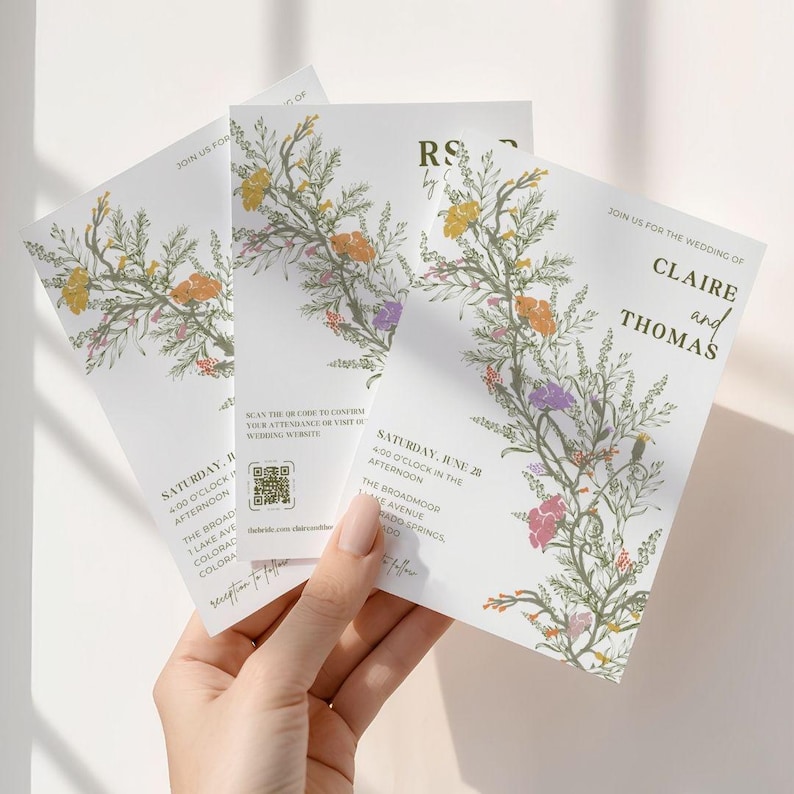 This is a lifestyle image of a womens hand holding three of the wedding invite templates up against a plain white wall. The invites are in a summery green, orange, yellows, purple, pinks against a bright white card.