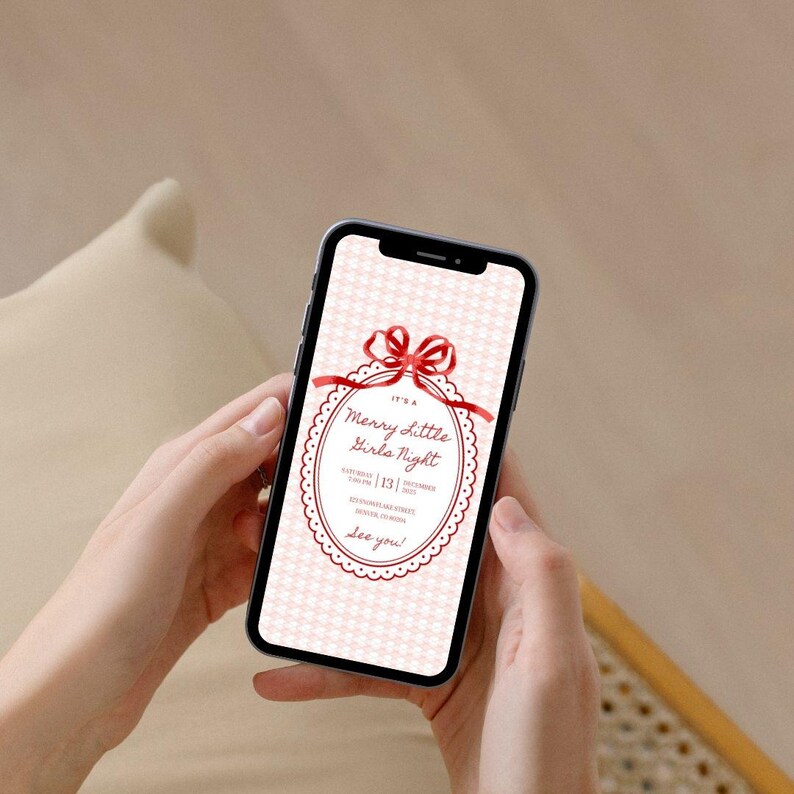 This is a lifestyle image mockup of a manicured pair of hands holding a phone. On the phone screen is a Christmas party invitation - this one is white and red.