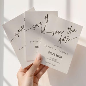 Puede incluir: Tres tarjetas marfil de "Save the Date" con una elegante escritura negra. Las tarjetas muestran "save the date", nombres y una fecha. Las tarjetas se sostienen en una mano, con el texto "Claire & Thomas" y la fecha "06.21.2028".