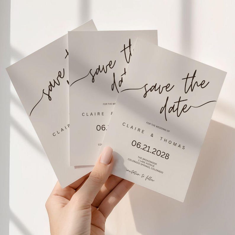 Puede incluir: Tres tarjetas marfil de "Save the Date" con una elegante escritura negra. Las tarjetas muestran "save the date", nombres y una fecha. Las tarjetas se sostienen en una mano, con el texto "Claire & Thomas" y la fecha "06.21.2028".