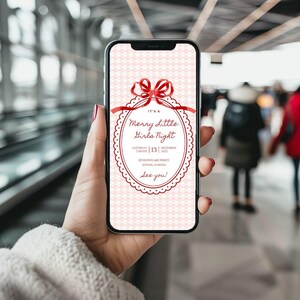 This is a lifestyle image mockup of a women's manicured hands holding a phone. The background is of a busy, urban area. In the center of the phone screen is a Christmas invitation. This invite has  red doodle font, white oval for the font to be centered in. There is a red shiny bow at the top of font.