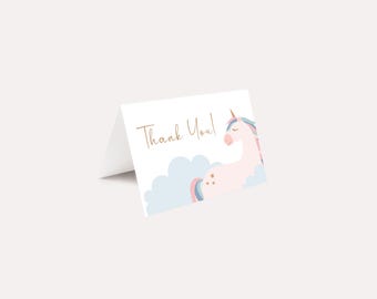 May include: A folded white card with the words "Thank You!" in gold script. The card features a pink unicorn with a rainbow mane and tail, resting on a blue cloud. The unicorn has a gold horn and two gold stars.