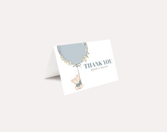 Peut inclure: Carte pliée blanche avec le texte "THANK YOU BEAR-Y MUCH!" en gris. Un ours de dessin animé est suspendu à un ballon bleu décoré de fleurs. La carte est une carte de remerciement ou de baby shower.