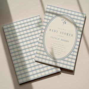 Op de afbeelding: Twee babyborrel uitnodigingen met een lichtblauw en wit ruitjespatroon. De uitnodiging rechts heeft een ovaal ontwerp met de woorden "BABY SHOWER" en details voor de babyborrel van Natalie Brooks.