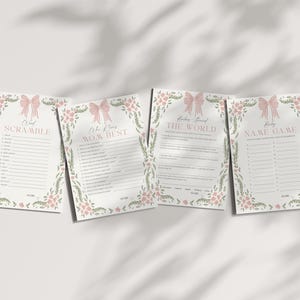 May include: Four baby shower game cards with floral and bow designs. The cards include games like "Word Scramble" and "Who Knows Mom Best". The cards are white with pink and green accents, and are arranged on a white surface.