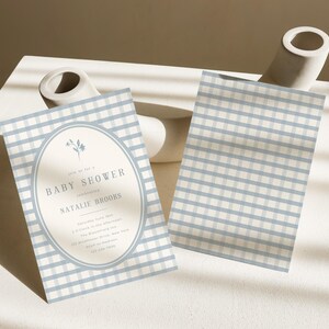 Op de afbeelding: Baby shower uitnodiging met een blauw en wit geruit patroon. De uitnodiging heeft een ovale lijst met bloemendetails en de tekst "Baby Shower" en evenementdetails. Een tweede kaart met hetzelfde patroon is ook zichtbaar.
