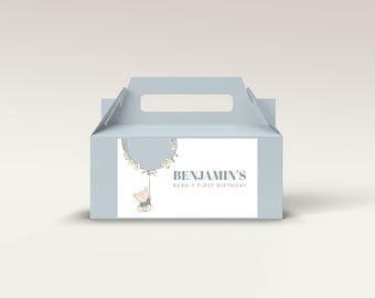 May include: A light blue party favor box with a handle. The box features a label with the text "BENJAMIN'S BEAR-Y FIRST BIRTHDAY". A cartoon teddy bear hangs from a balloon illustration.
