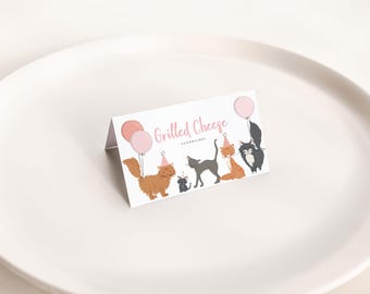 Könnte beinhalten: Eine gefaltete Karte mit dem Text "Grilled Cheese Sandwiches" und Illustrationen von Katzen mit Partyhüten und Luftballons. Die Karte hat rosa und orangefarbene Akzente und liegt auf einem weißen Teller.