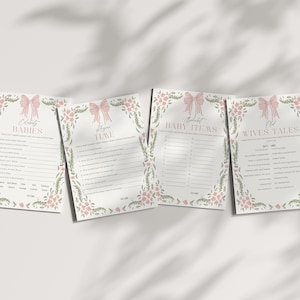May include: Four baby shower game cards with pink bow and floral designs. The cards include games like "Celebrity Babies," "Guess the Baby Items," and "Old Wives Tales." The cards are on a white surface with shadows.