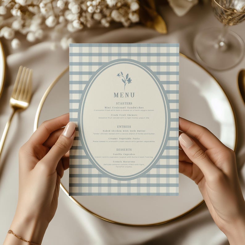 Op de afbeelding: Een menukaart met een blauw en wit geruit vichy-patroon. Het menu heeft een ovale lijst met bloemmotieven en het woord "MENU" bovenaan. Het menu bevat voorgerechten, hoofdgerechten en desserts.