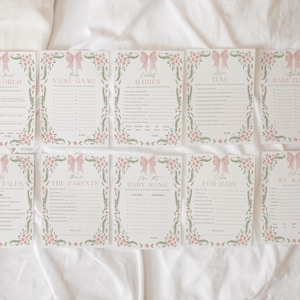May include: A set of ten baby shower game cards. Each card features a pink bow and floral border. The titles include "The World", "Name Game", "Babies", "Time", "Baby Items", "Wives Tales", "The Parents", "Baby Song", "For Baby", and "My Mama".