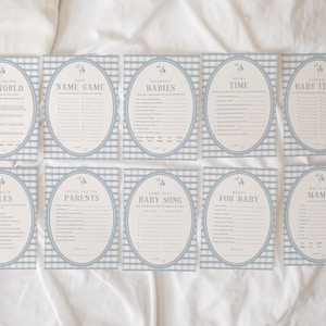 Op de afbeelding: Een set van tien babyshower-spelkaarten. Elke kaart heeft een blauw-wit geruite vichy-rand en een ovale lijst. De kaarten hebben titels als "De Wereld", "Naamspel" en "Babyartikelen".