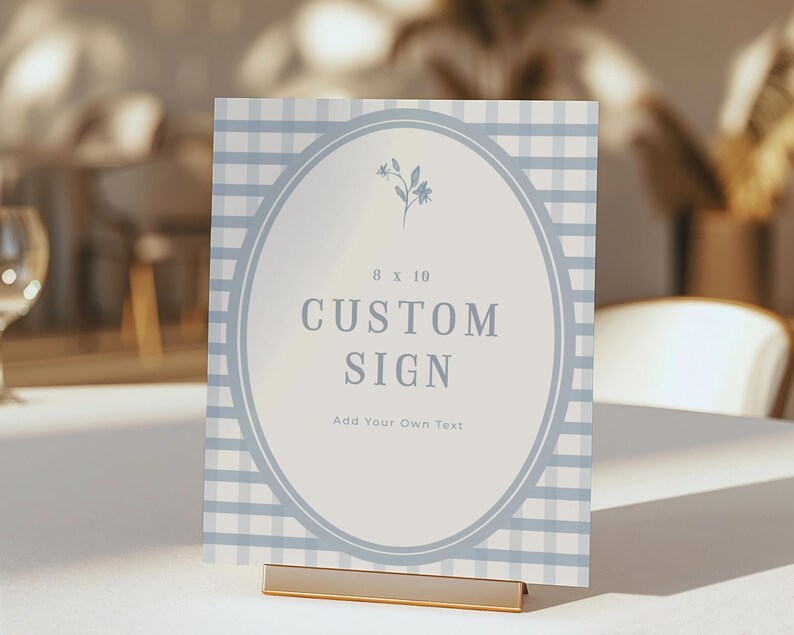 Op de afbeelding: Een aangepast bord met een lichtblauwe gingham patroon achtergrond. Het bord heeft een ovale midden met de woorden "CUSTOM SIGN" in een vet lettertype. Het bord is 20,3 x 25,4 cm en wordt vastgehouden door een goudkleurige metalen standaard.