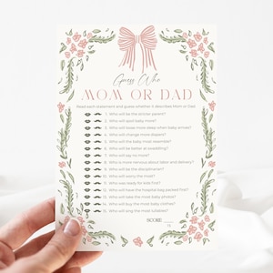 May include: A cream-colored baby shower game card with the text "Guess Who Mom or Dad". The card features a pink bow and floral border. The game includes questions to determine who will be the stricter parent.