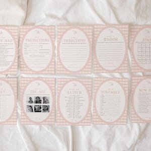 May include: Ten pink and white game cards are displayed, each with a different title such as "Mom or Dad" and "Bingo." The cards have an oval design with floral details and spaces for game play. They are arranged on a white surface, with a gingham-style background.
