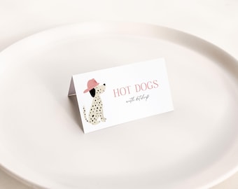 May include: A white card with the words "HOT DOGS with ketchup" and a cartoon Dalmatian wearing a pink hat. The card is on a white plate.