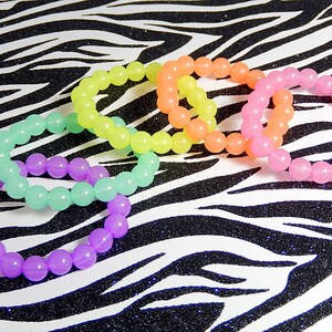 May include: Five colorful bracelets made of round beads. The bracelets are in shades of purple, green, yellow, orange, and pink. The bracelets are arranged in a circle on a black and white zebra print background.