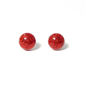 May include: A pair of red glitter stud earrings. The earrings are small and round, and they have a shiny, sparkly finish.