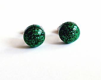 May include: A pair of green glitter stud earrings. The earrings are round and have a silver backing.