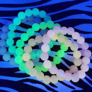 May include: Three glow-in-the-dark bracelets made of round beads. The bracelets are layered on top of each other. The top bracelet is green, the middle bracelet is yellow, and the bottom bracelet is pink.