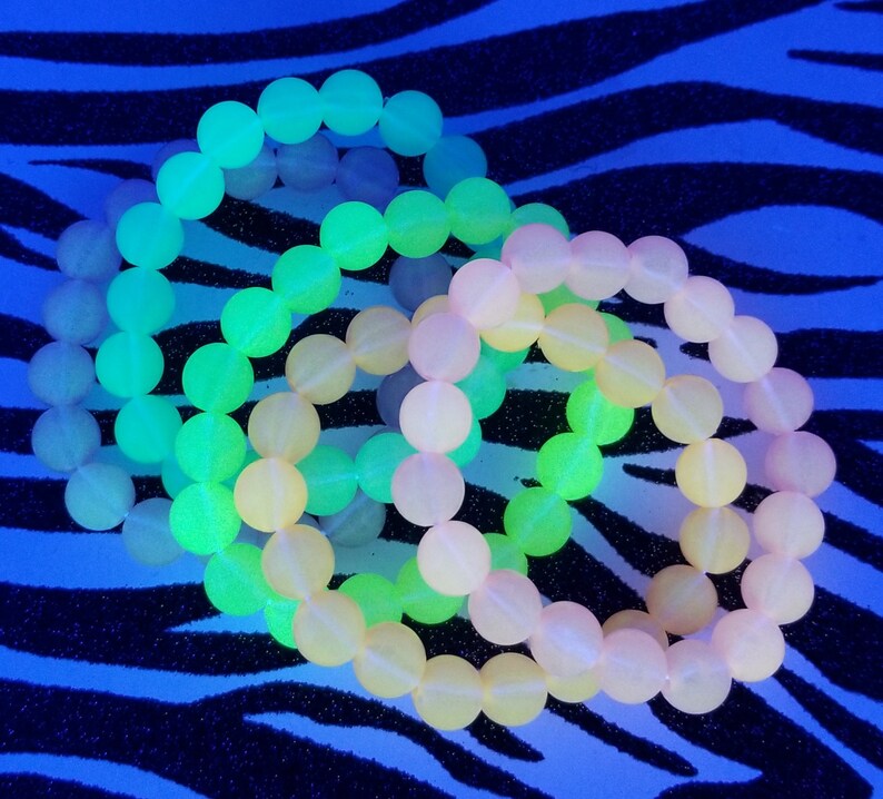 May include: Three glow-in-the-dark bracelets made of round beads. The bracelets are layered on top of each other. The top bracelet is green, the middle bracelet is yellow, and the bottom bracelet is pink.
