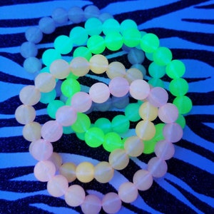 May include: Three glow-in-the-dark bracelets in pink, yellow, and green. The bracelets are made of round beads and are stacked on top of each other.