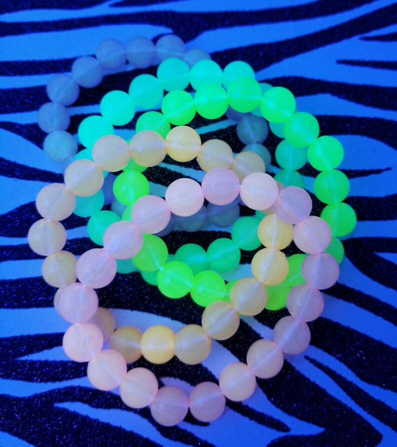 May include: Three glow-in-the-dark bracelets in pink, yellow, and green. The bracelets are made of round beads and are stacked on top of each other.