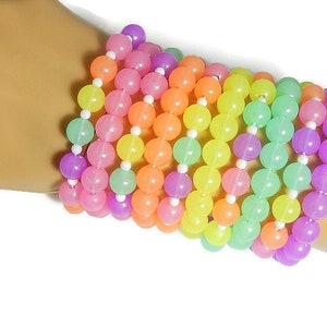 May include: A stack of colorful bracelets made of pastel-colored beads. The bracelets are made of pink, orange, yellow, green, and purple beads.
