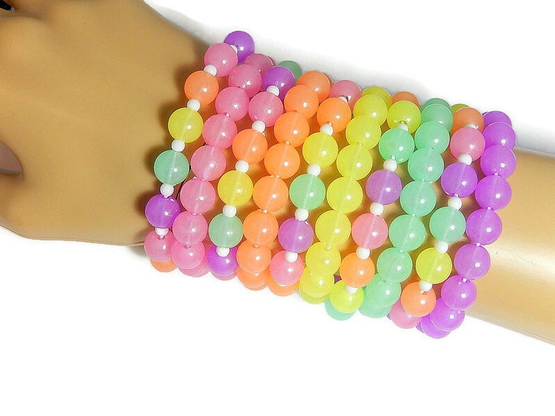 May include: A stack of colorful bracelets made of pastel-colored beads. The bracelets are made of pink, orange, yellow, green, and purple beads.