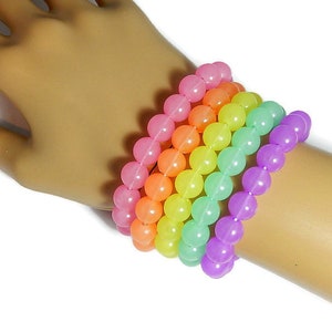 May include: A set of six colorful bracelets made of round, translucent beads. The bracelets are stacked on a person's wrist and feature a rainbow color scheme, starting with pink and transitioning to purple.