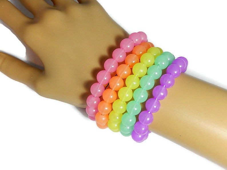 May include: A set of six colorful bracelets made of round, translucent beads. The bracelets are stacked on a person's wrist and feature a rainbow color scheme, starting with pink and transitioning to purple.
