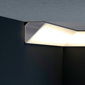 Può includere: Un moderno apparecchio di illuminazione a soffitto geometrico. L'apparecchio è di colore bianco brillante, con un design angolare, montato nell'angolo di una stanza. La luce emette un bagliore caldo, in contrasto con le pareti e il soffitto blu scuro.