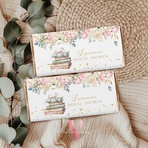 Puede incluir: Dos envoltorios rectangulares de barra de caramelo con un diseño floral. Los envoltorios presentan una pila de libros atados con un lazo, rodeados de rosas rosas y blancas. El texto "Laurencia's Bridal Shower" está escrito en una elegante escritura.