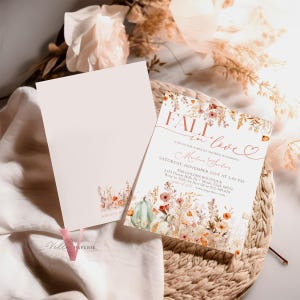 May include: Fall in love bridal shower invitation with a watercolor floral design featuring pumpkins, leaves, and flowers in shades of orange, pink, and green. The text reads "Fall in love" with a heart and "Join us for a bridal shower honoring Madeline Santos".
