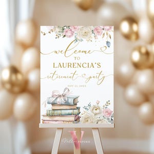 May include: A white retirement party sign with gold script that reads "Welcome to Laurencia's Retirement Party." The sign features watercolor flowers, books, and a bow. The sign is displayed on a white easel.