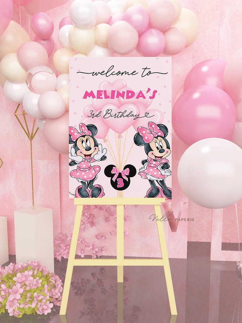May include: A pink birthday welcome sign on a yellow easel, featuring Minnie Mouse illustrations and the text "welcome to MELINDA'S 3rd Birthday". Pink and white balloons decorate the background.