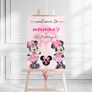 May include: A pink birthday welcome sign featuring Minnie Mouse illustrations. The sign reads "welcome to Melinda's 3rd Birthday" and includes pink balloons. The sign is displayed on a wooden easel, suitable for a third birthday party.