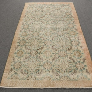 May include: Rectangular area rug with a beige border and a central pattern of floral and geometric designs in shades of beige, brown, and teal. The rug has a distressed, vintage appearance.