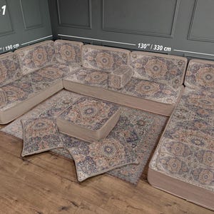 以下が含まれることがあります： U字型のコーナーソファセット、お揃いのラグとクッション付き。ソファはベージュで、青、茶色、クリーム色の模様があります。コーナーソファは幅330cm、長さ190cmです。ラグとクッションは同じ模様です。