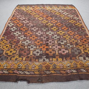 May include: A rectangular, vintage rug with a geometric pattern in shades of brown, orange, yellow, and white. The rug features a detailed border with a repeating design. The rug is likely made of wool or a similar natural fiber.