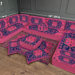 May include: A pink sectional sofa with a patterned rug and matching pillows. The sofa is 130 inches (330 cm) long and 75 inches (190 cm) wide, with a depth of 28 inches (70 cm). The rug and pillows feature a blue and pink geometric design.