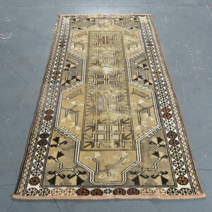 May include: A rectangular area rug featuring a central tan field with dark brown and black geometric patterns. The border displays a repeating motif of circular shapes in brown, black, and white, framing the intricate linear designs throughout.