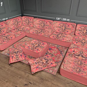 May include: A U-shaped sectional sofa set with a matching rug and ottoman. The set is upholstered in a patterned fabric with shades of red, pink, and blue. The sofa measures 130 inches (330 cm) long and 75 inches (190 cm) wide. The ottoman is 28 inches (70 cm) wide.
