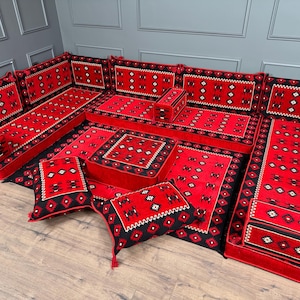 May include: A red and black floor seating set with a geometric pattern. The set includes multiple cushions, a long bench, and a rectangular ottoman. The design features a repeating pattern of diamonds and other shapes.