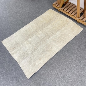 May include: A rectangular area rug featuring a woven texture in a neutral beige and off-white color palette. The rug displays a subtle, faded pattern across its surface, with a consistent weave throughout the entire piece, showcasing a flat construction.