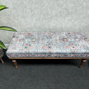 May include: A patterned ottoman with a wooden frame and legs. The ottoman has a light blue, pink, and white floral pattern.