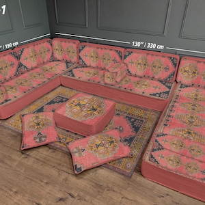 May include: U-shaped sectional sofa set in a coral hue, featuring intricate patterned upholstery. The set includes a sofa, ottoman, and throw pillows, all with a matching design. The sofa measures 130 inches (330 cm) long and 75 inches (190 cm) wide. The pillows are 28 inches (70 cm) wide.
